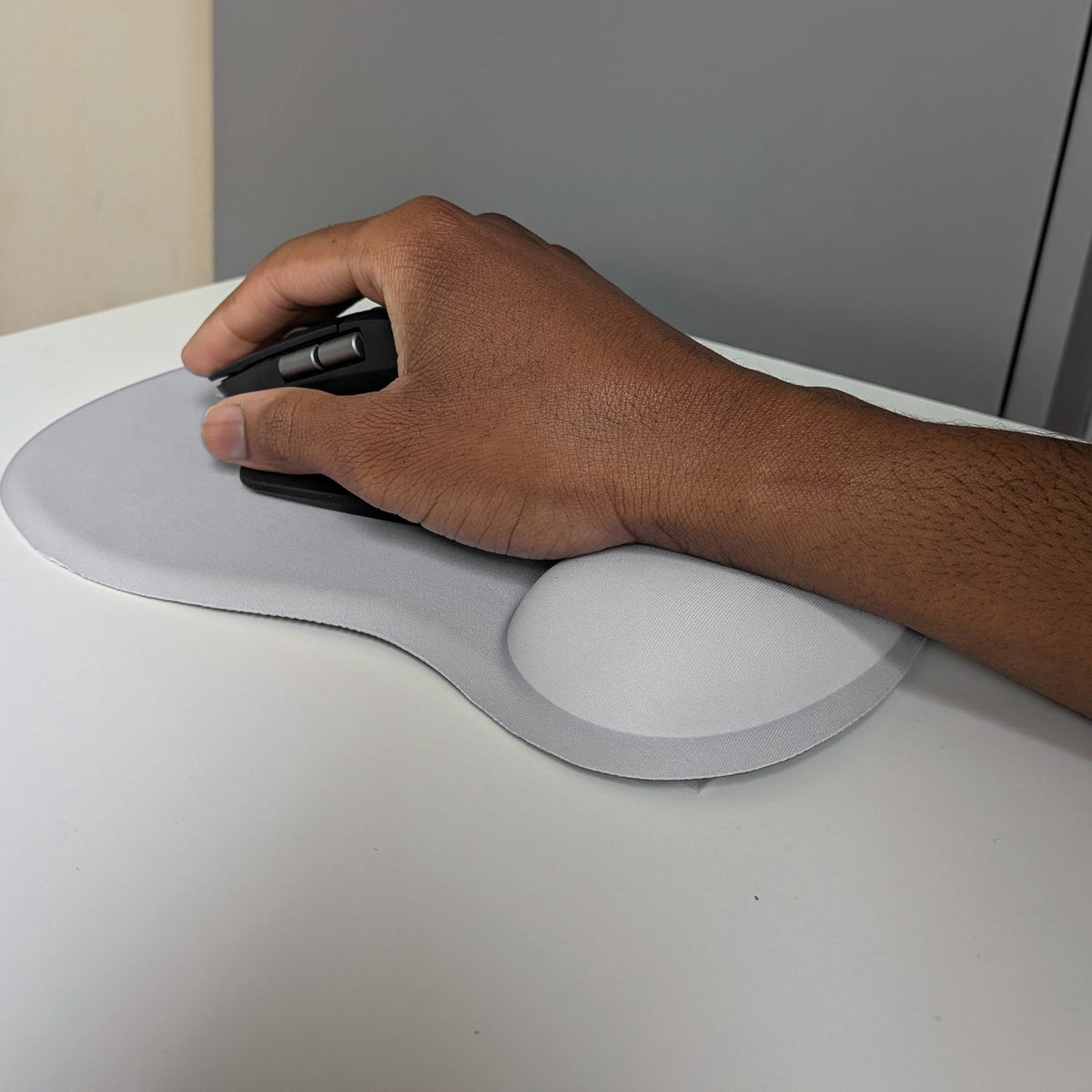 Main sur une souris verticale, poignet posé sur le repose-poignet du tapis de souris ergonomique Ergozone gris